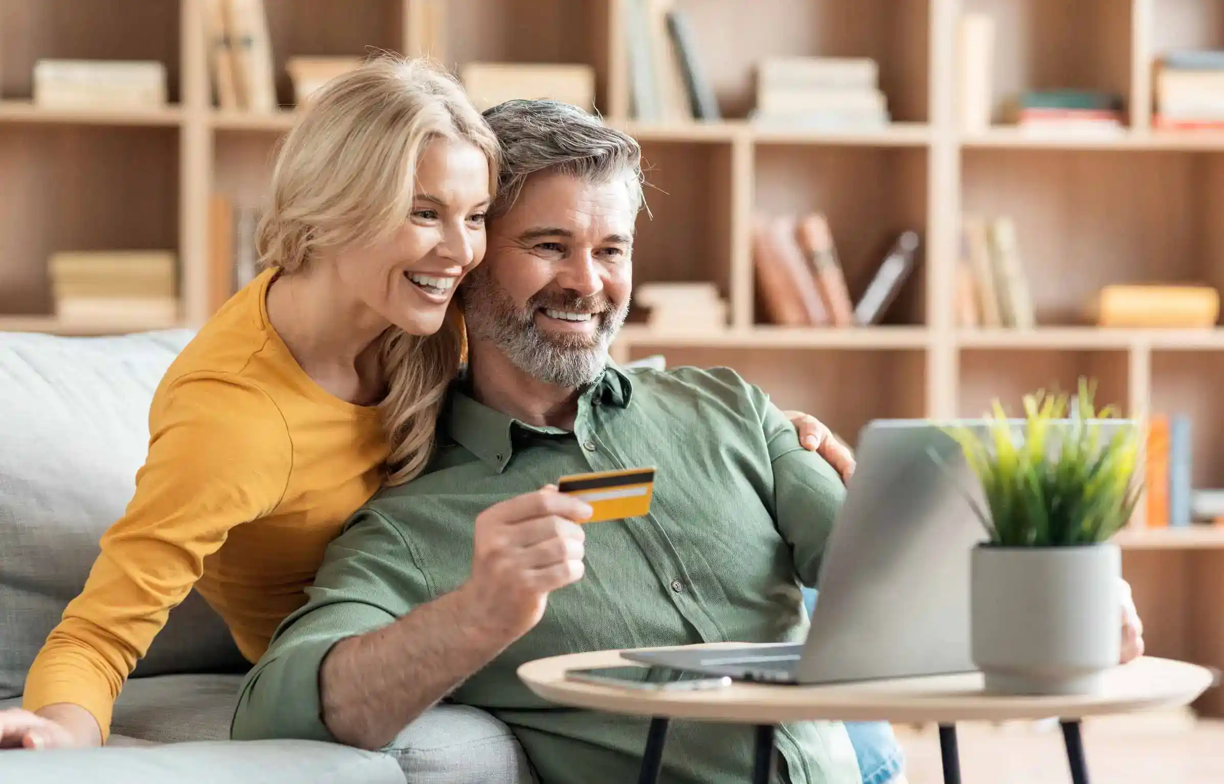 A retired couple using a card on a laptop for payments.