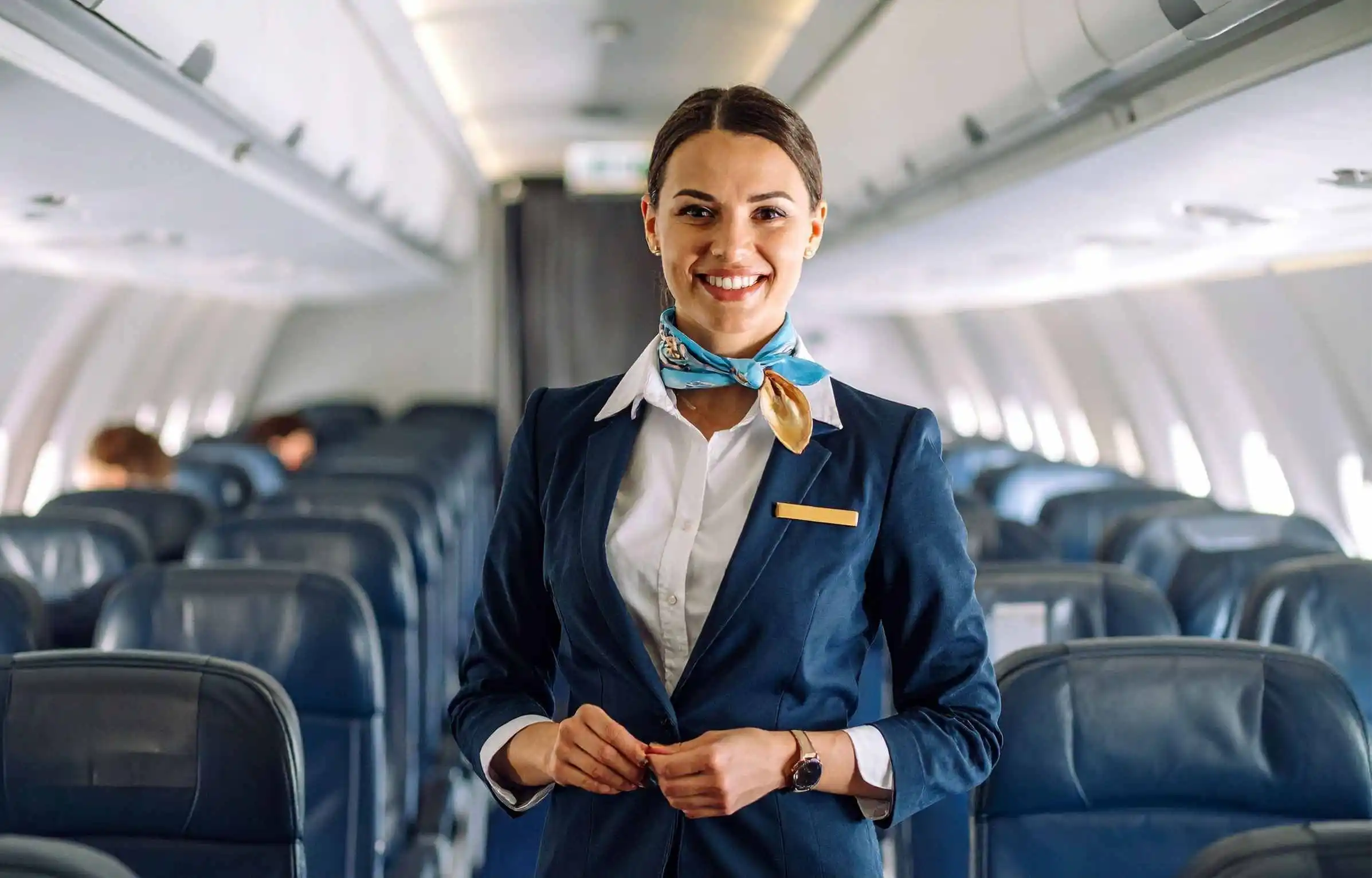 Smiling Alaska Airlines flight attendant standing in aircraft aisle with passengers in background.