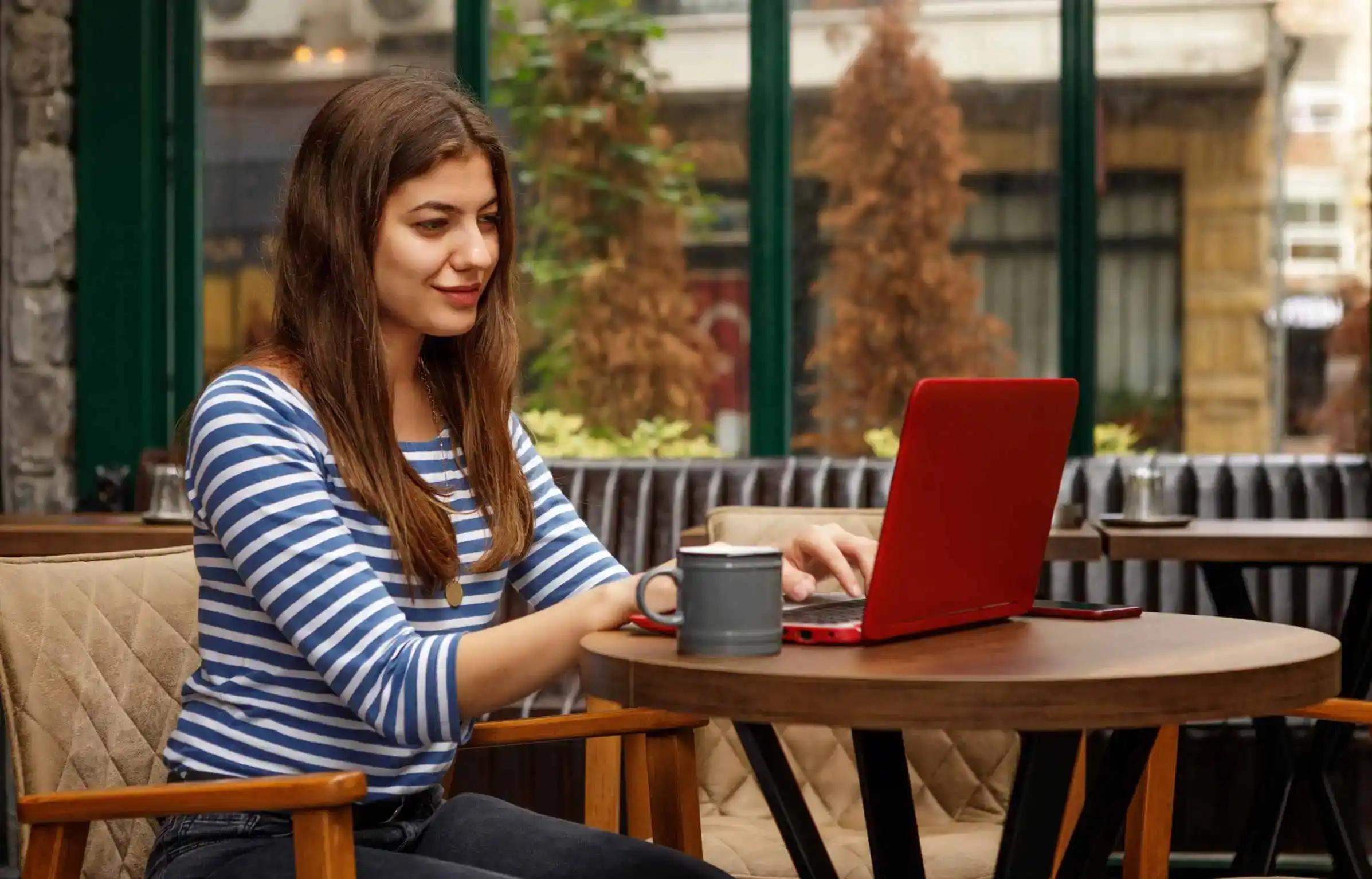 A woman is working on a laptop at a café with a coffee mug beside her.