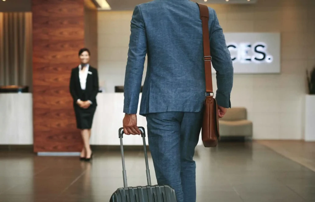 An executive traveler in a tailored blue suit pulls a roller suitcase into a premium hotel lobby, utilizing IHG One Rewards points stacked for an extended corporate relocation stay.