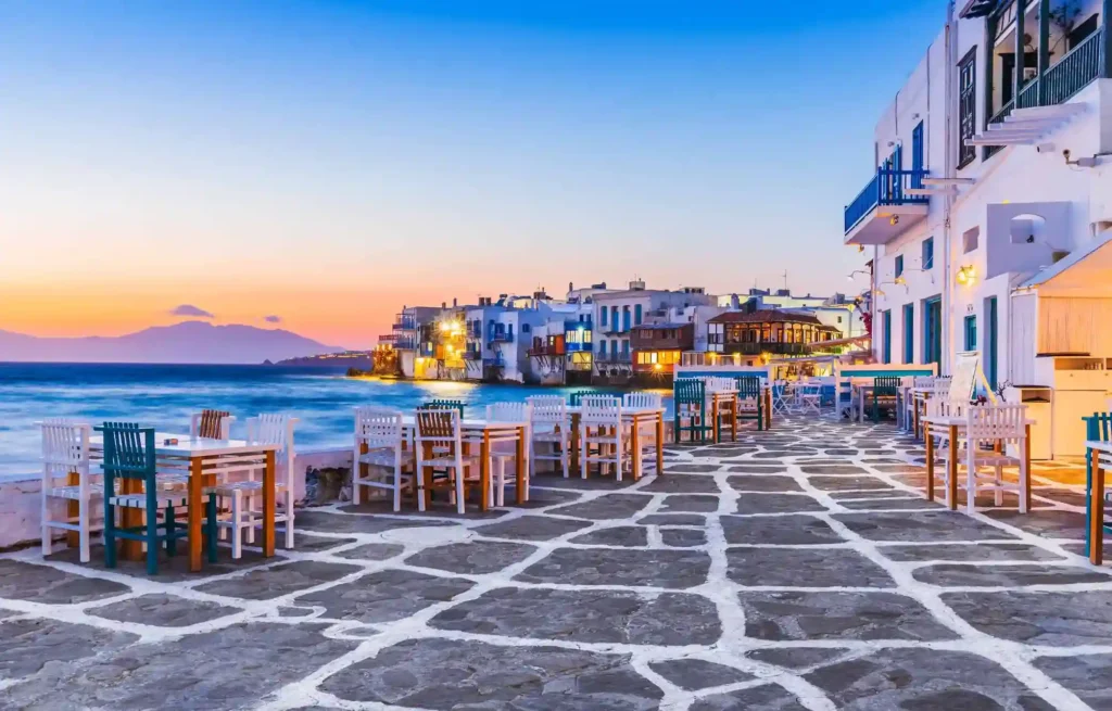 Greek seaside town at sunset with white buildings and ocean views.