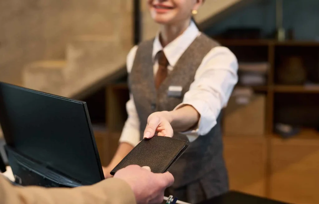 A hotel guest hands an identification document to a smiling receptionist at check-in to activate the IHG One Rewards 3X points promotion on a paid luxury stay.