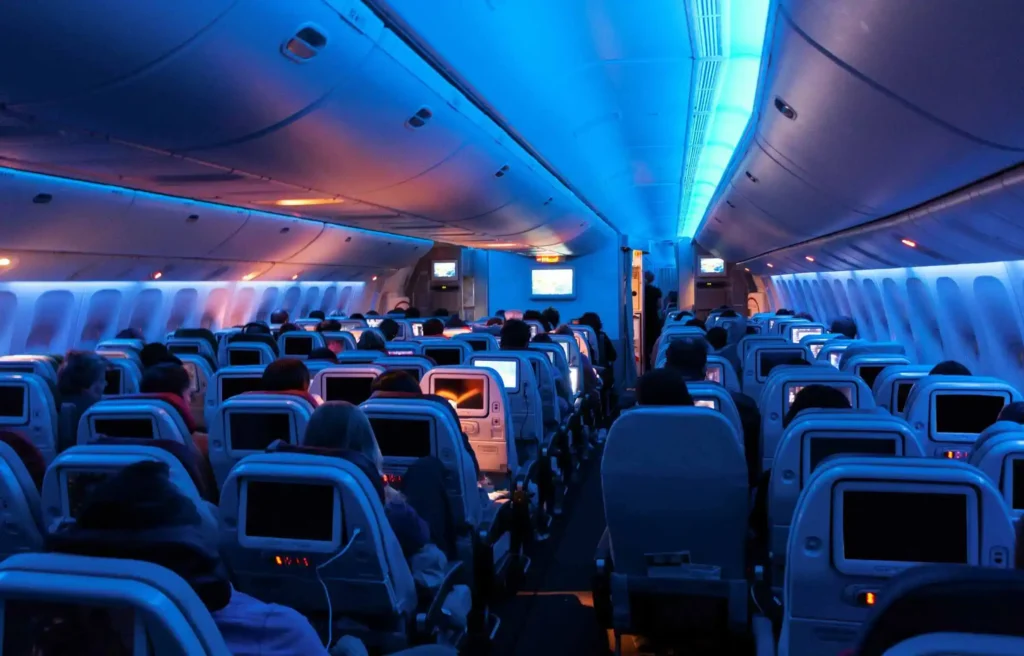 Airplane cabin with passengers seated under blue cabin lighting during a flight, american miles vs loyalty points.