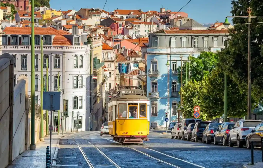 Yellow Lisbon tram travelling through a sunny street of colourful historic homes.