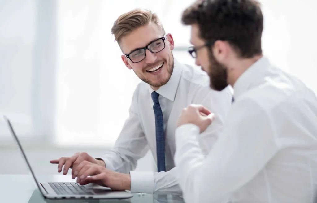 Two smiling coworkers discuss AI in corporate relocation during a bright office meeting.