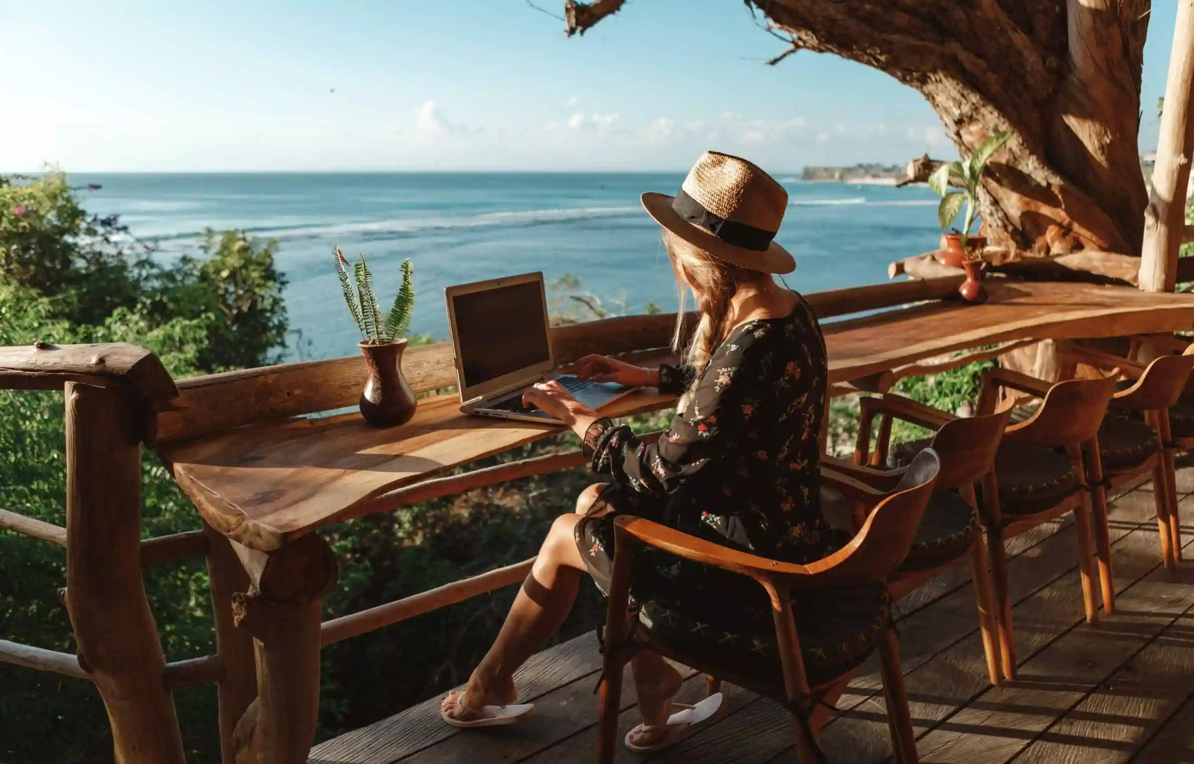 Digital nomad working on a laptop from a wooden terrace overlooking the ocean.