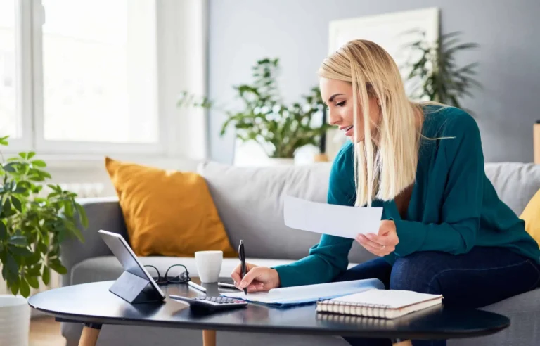 A woman reviewing tax documents at home with a calculator and tablet.