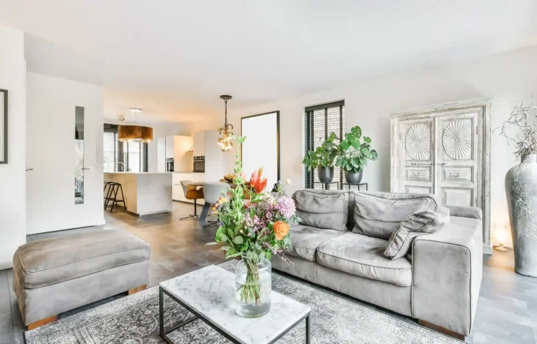 Bright furnished corporate apartment with a gray sofa, modern kitchen, plants, and fresh flowers.