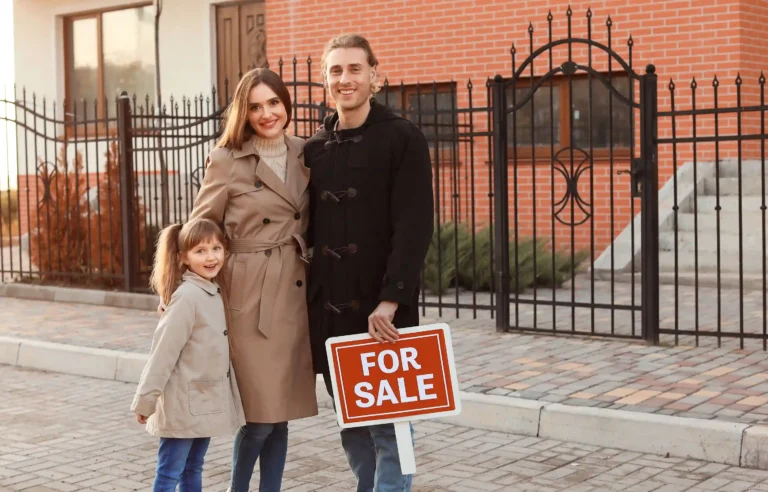 Family stands outside their home with a for-sale sign before relocating.