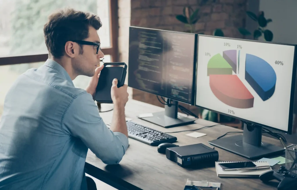 Man reviewing software engineer relocation data, code, and a pie chart on dual desktop monitors.