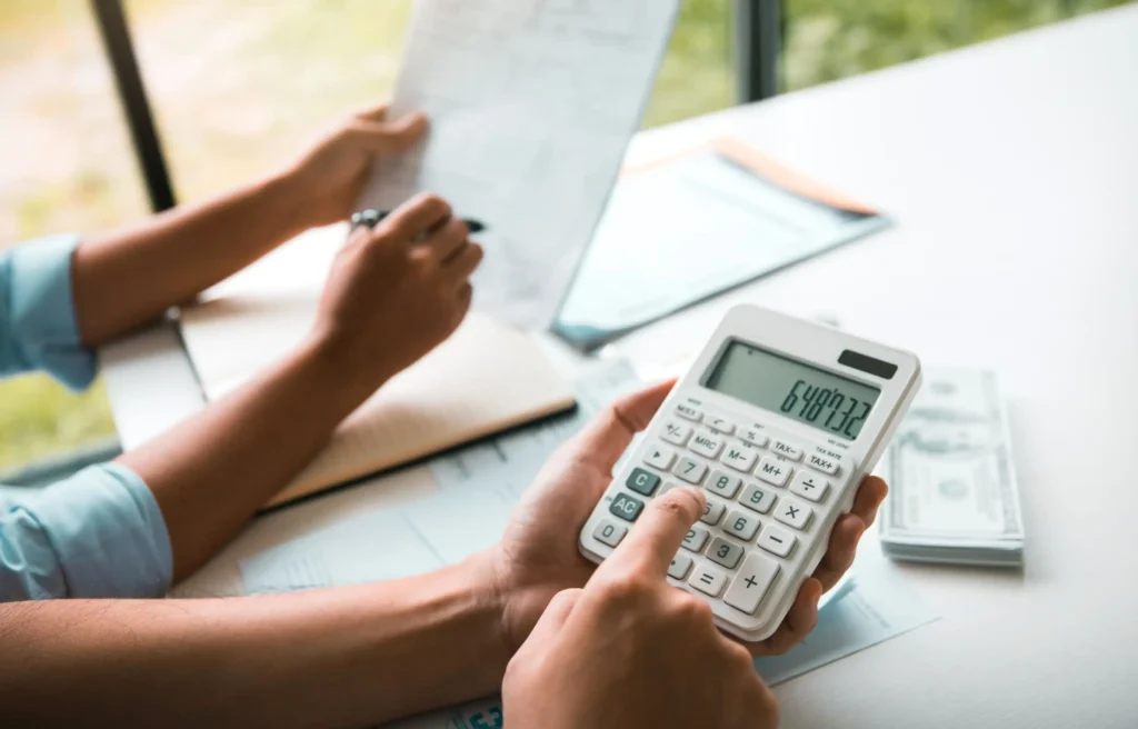 Person calculates employee relocation costs beside documents, a laptop, and cash.