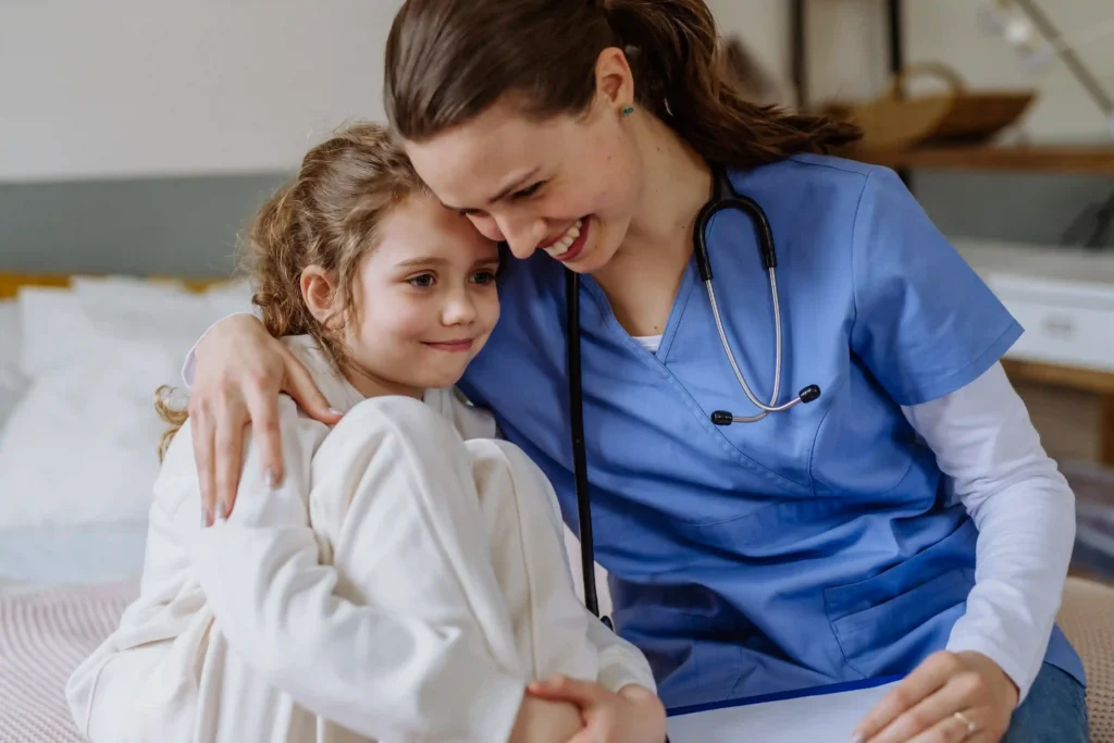 Relocating nurse in blue scrubs comforting her young child while preparing for a new healthcare role.