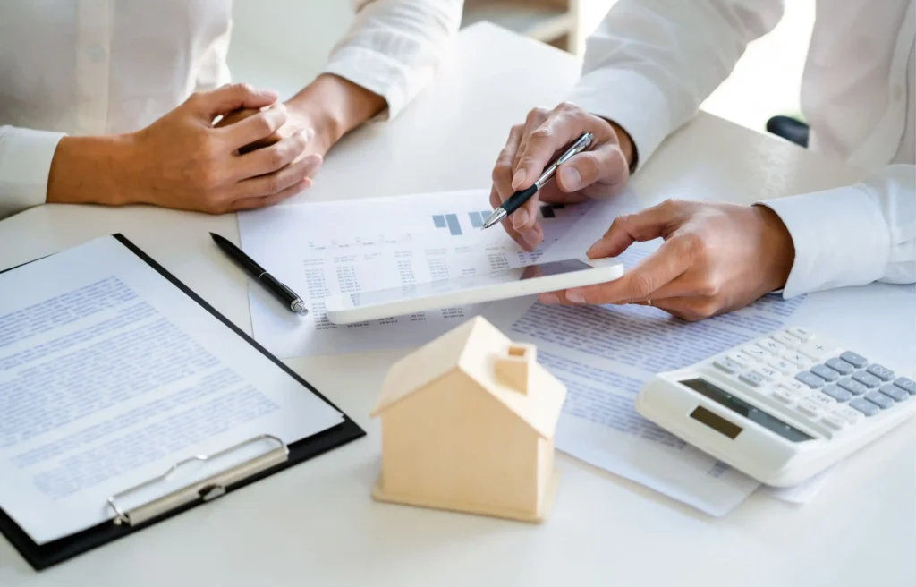 Advisor reviews relocation home sale programs with a client beside a model house and calculator.