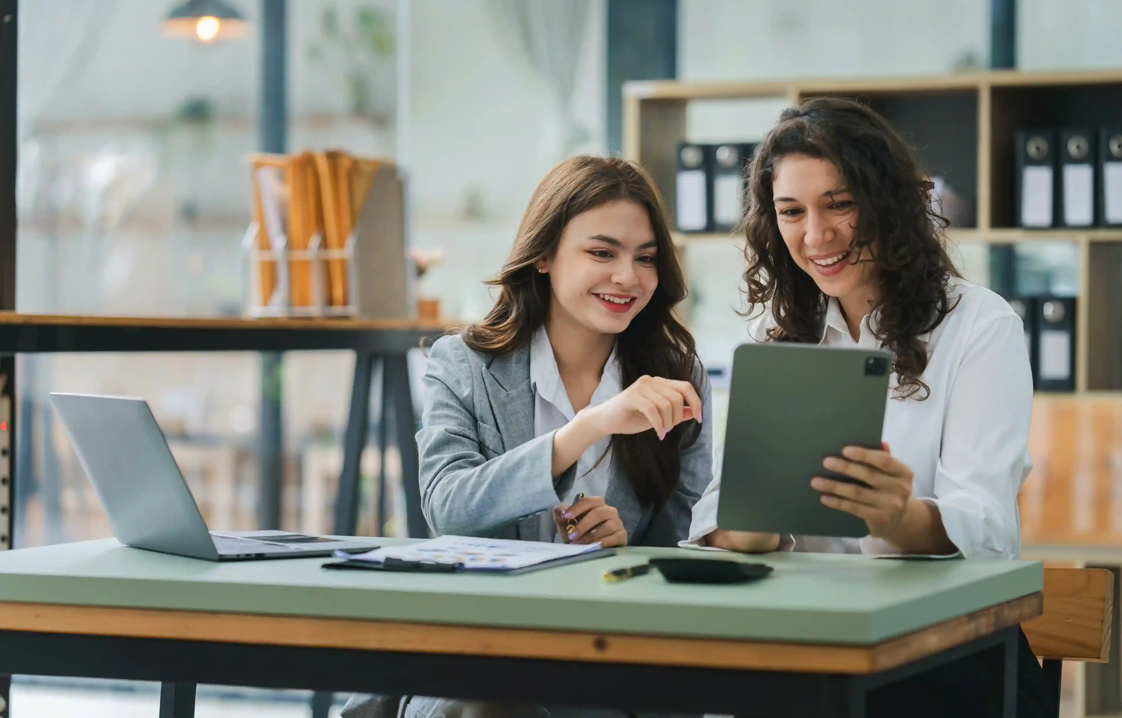 Two HR professionals review employee relocation costs on a tablet in a modern office.