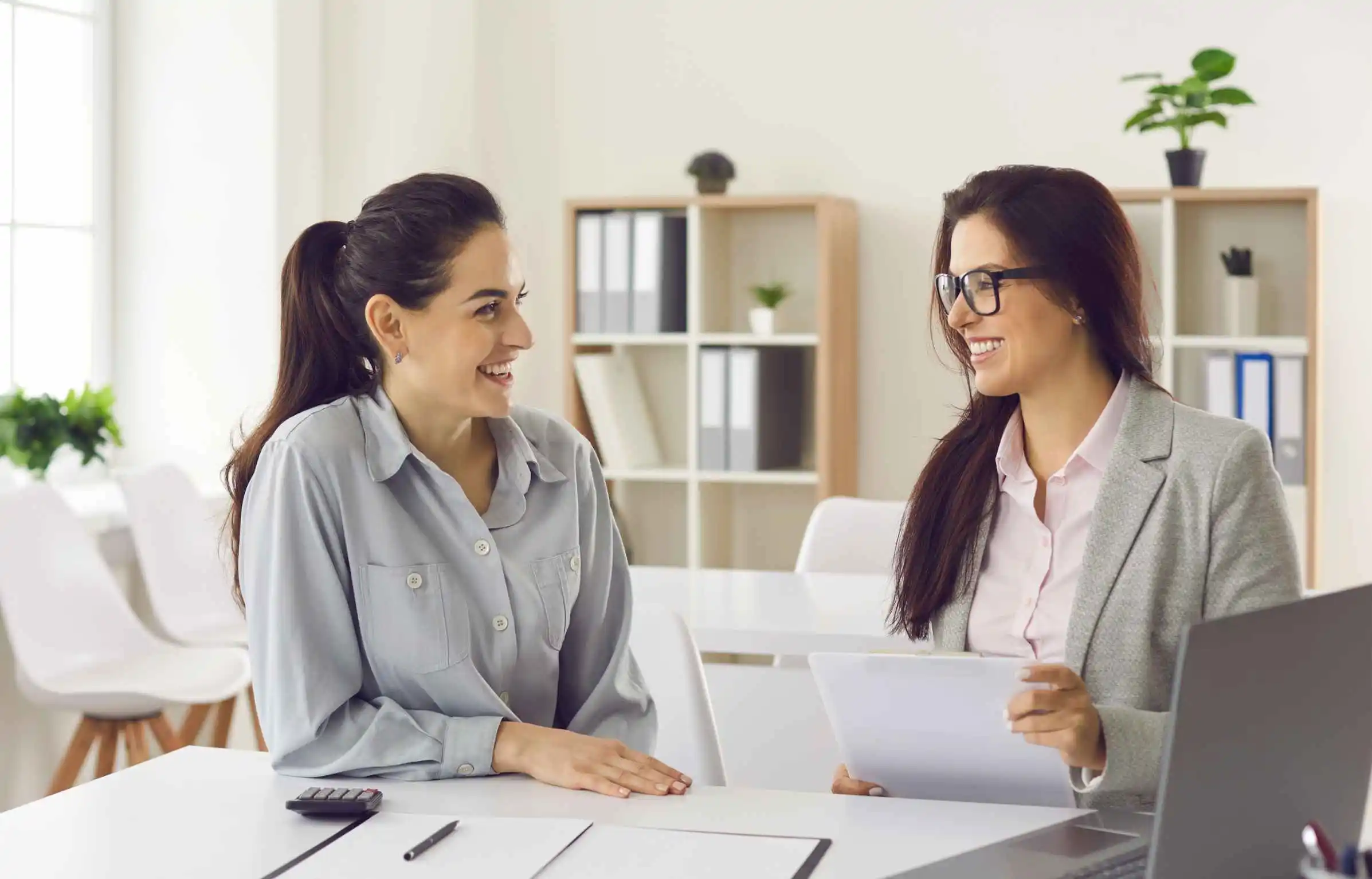 Two women review documents and discuss a relocation offer in a bright office.