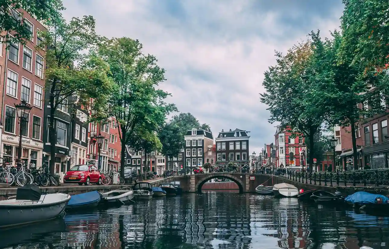 Amsterdam canal lined with historic houses, bicycles, and boats under a cloudy sky.