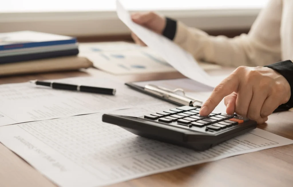 Calculator and paperwork used to review first paycheck after relocation taxes and costs.