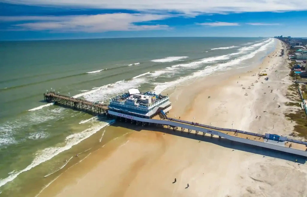 Daytona Beach, Florida aerial view of the sandy coast, ocean waves, and beachfront pier.