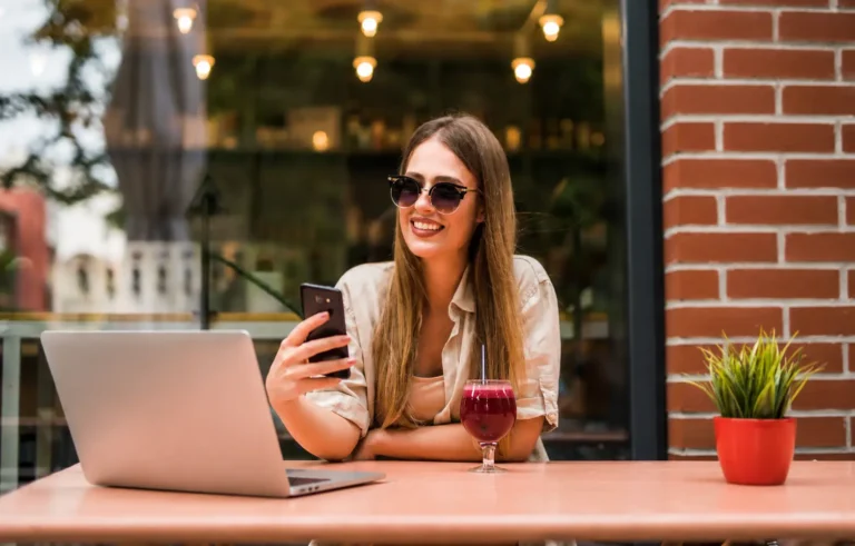 Digital nomad woman using a laptop and smartphone at an outdoor café.