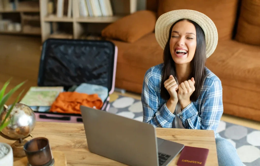 Woman researching long-distance moving plans on a laptop beside an open suitcase and passport.