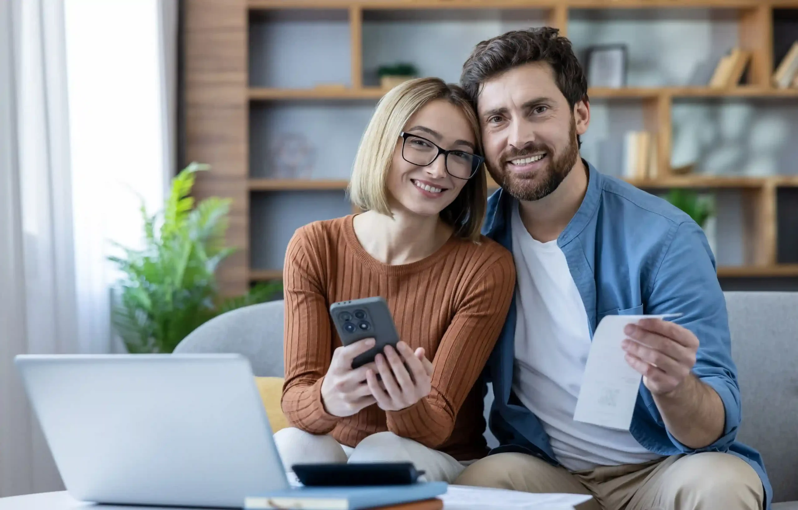 Couple reviewing a relocation receipt with a phone and laptop while managing moving expenses.