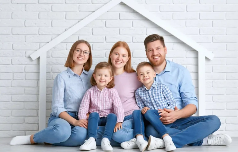 Family preparing for split family relocation while sitting together in front of a house-shaped backdrop.