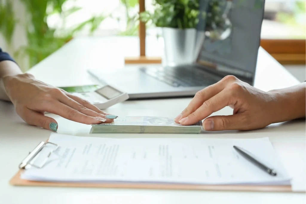 Hands exchanging cash during a rental relocation security deposit payment with paperwork and a laptop on the desk.