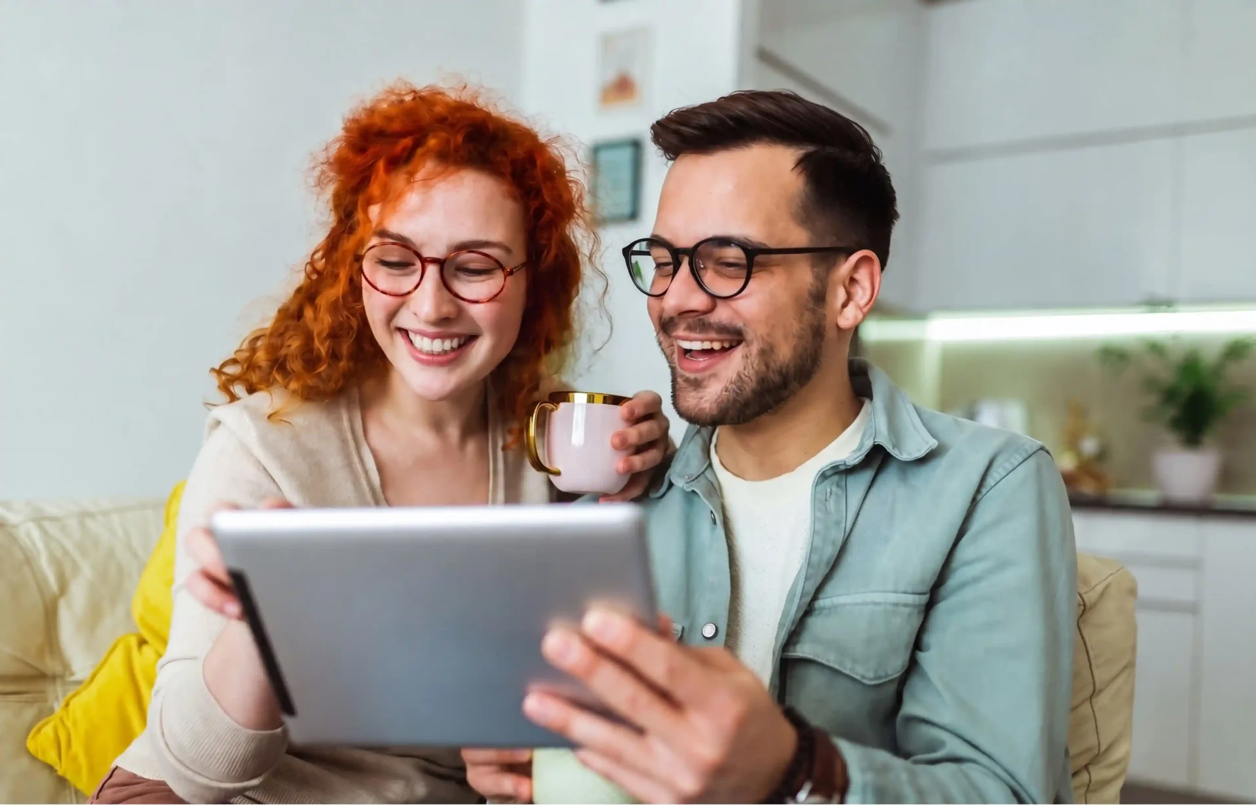 Happy couple sitting at home and using a tablet together while enjoying coffee.