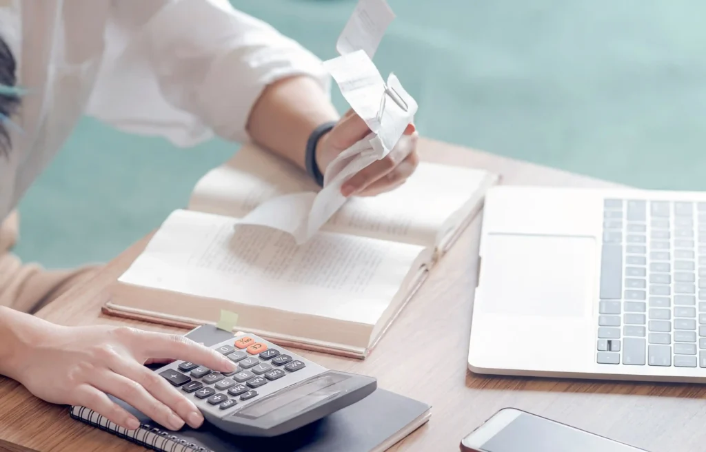 Person organizing relocation receipts with a calculator and laptop while tracking moving expenses.