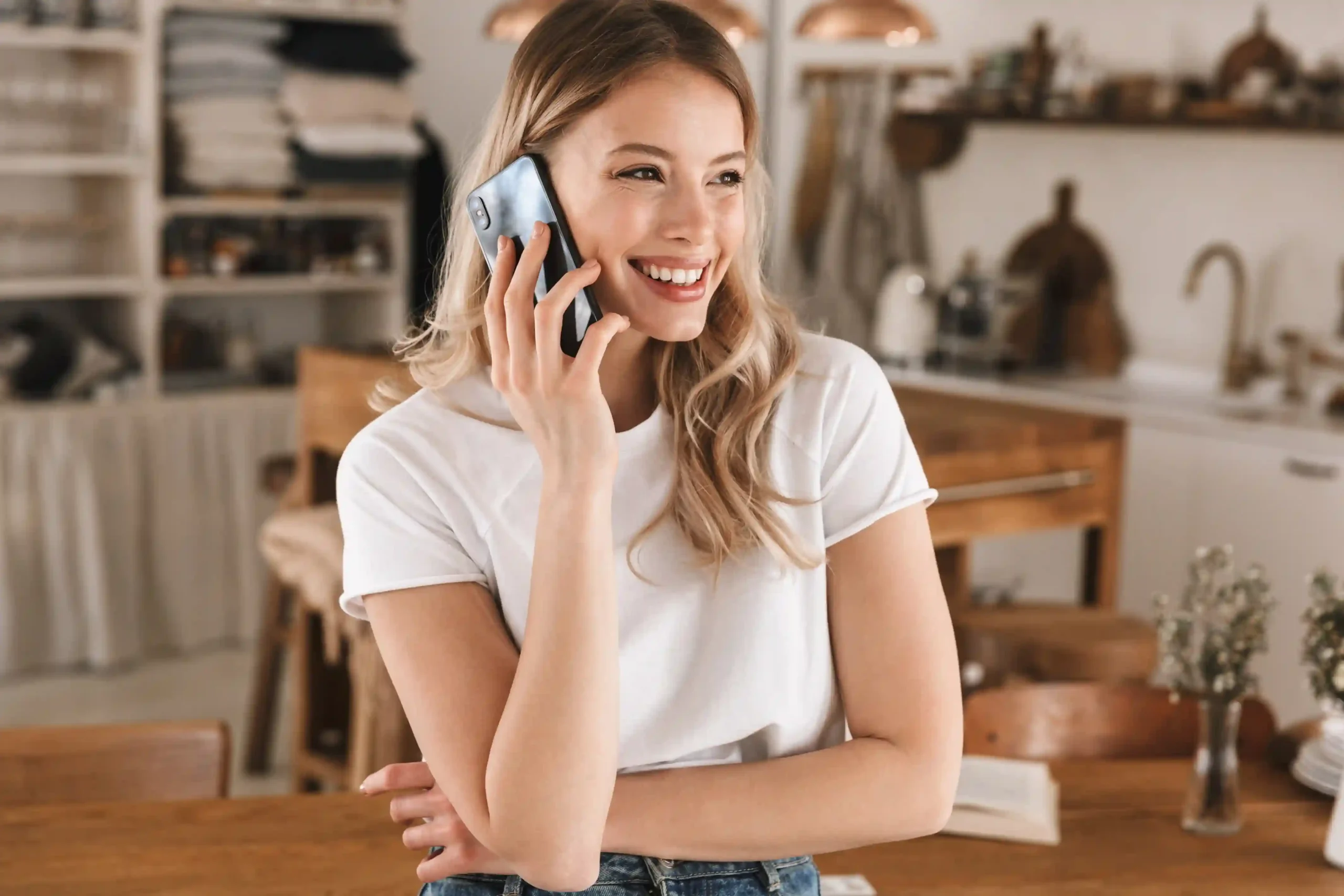 Smiling woman talking on a smartphone in a bright kitchen while discussing plans for an upcoming relocation.