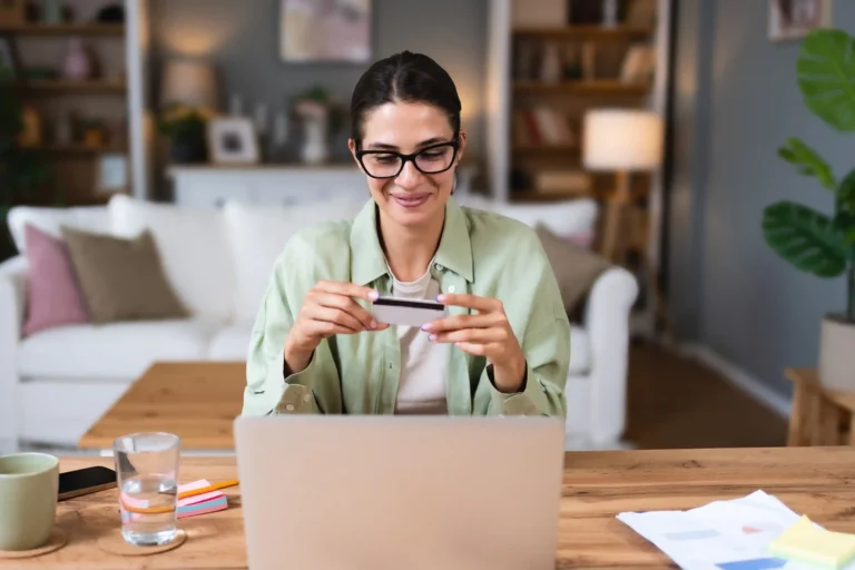 Woman holding a bank card while using a laptop to manage relocation security deposit payments.