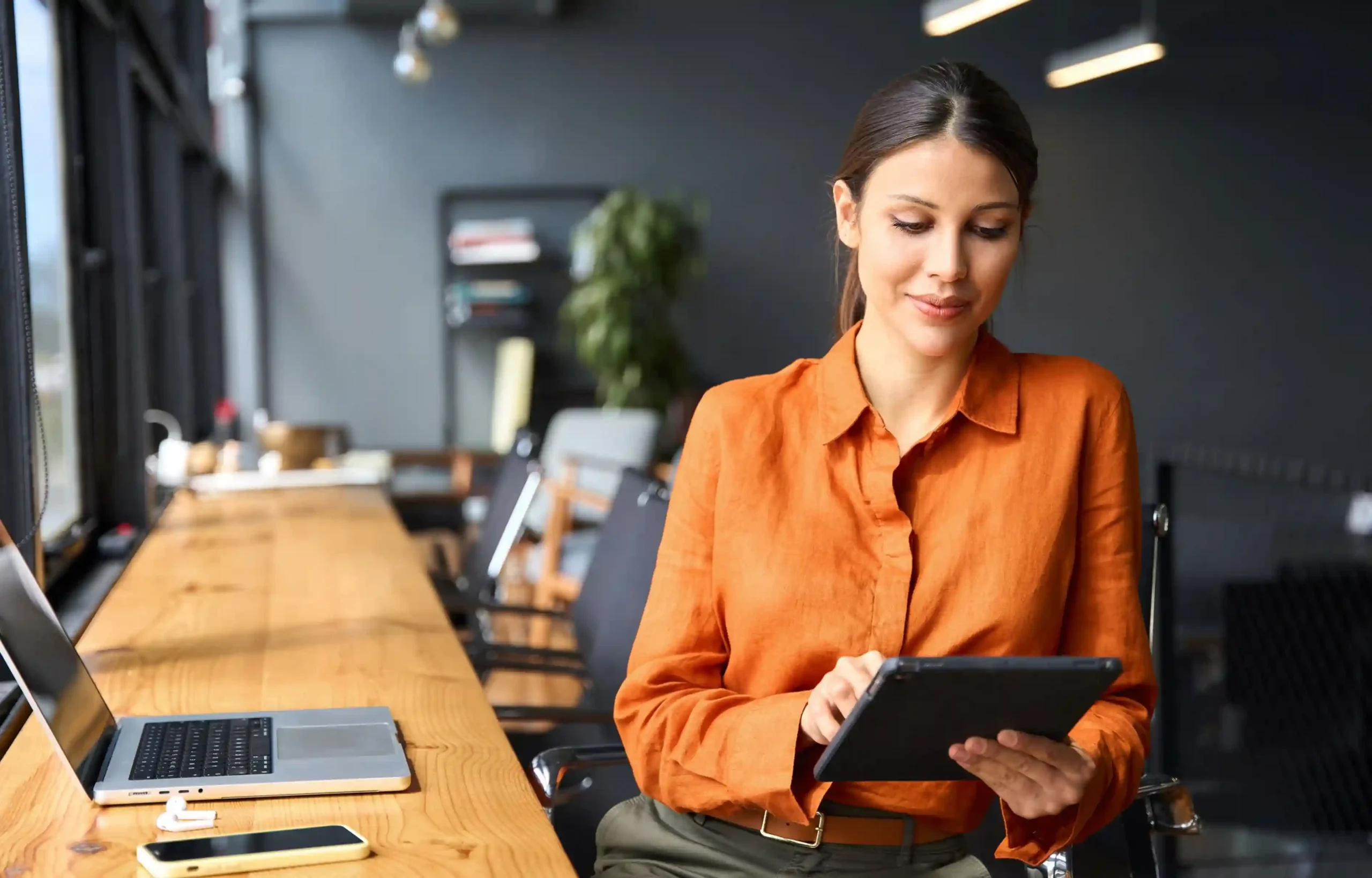 Woman using a tablet at a modern office desk with a laptop and smartphone.