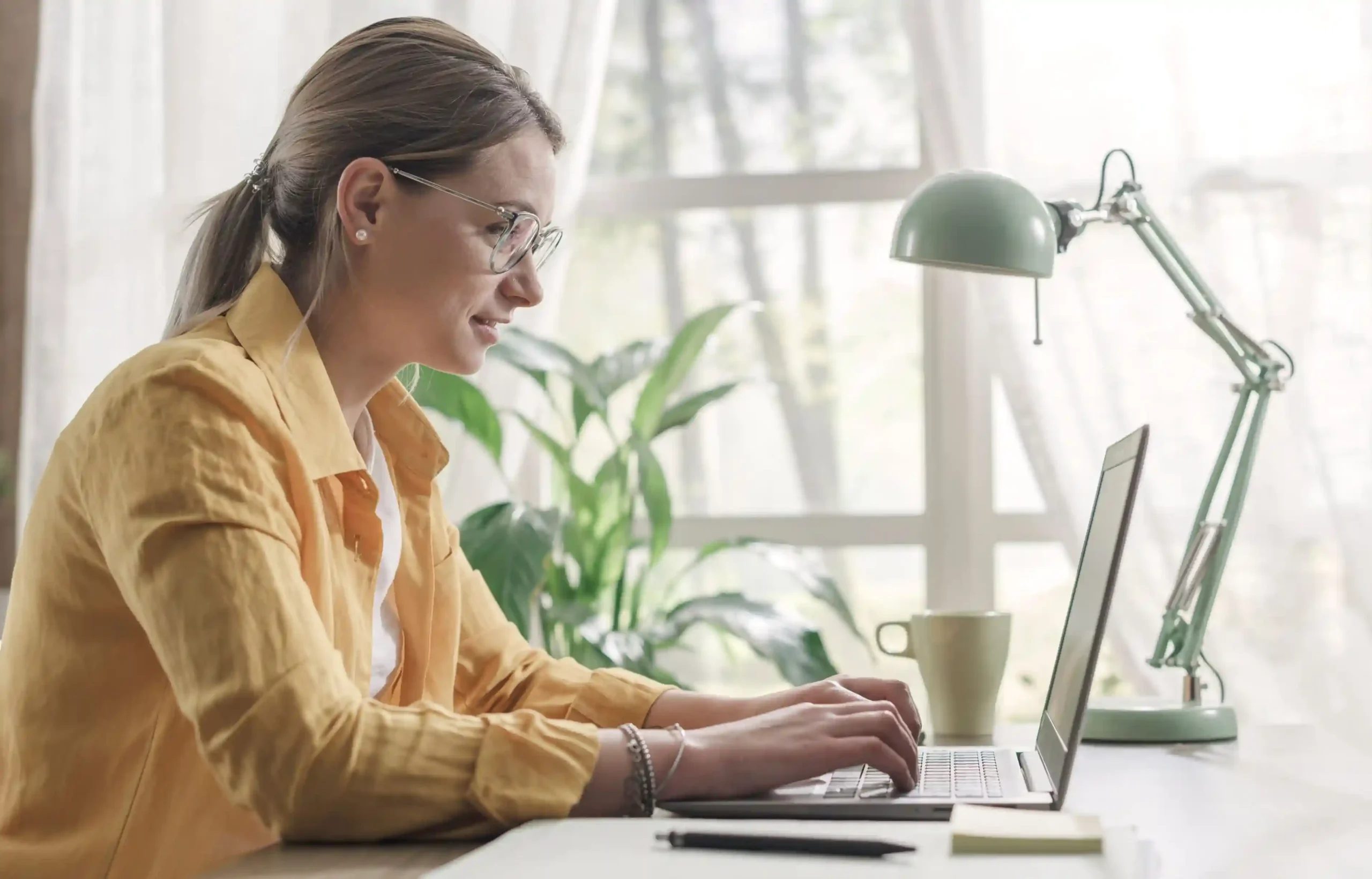 Woman working remotely on a laptop at a bright home desk.
