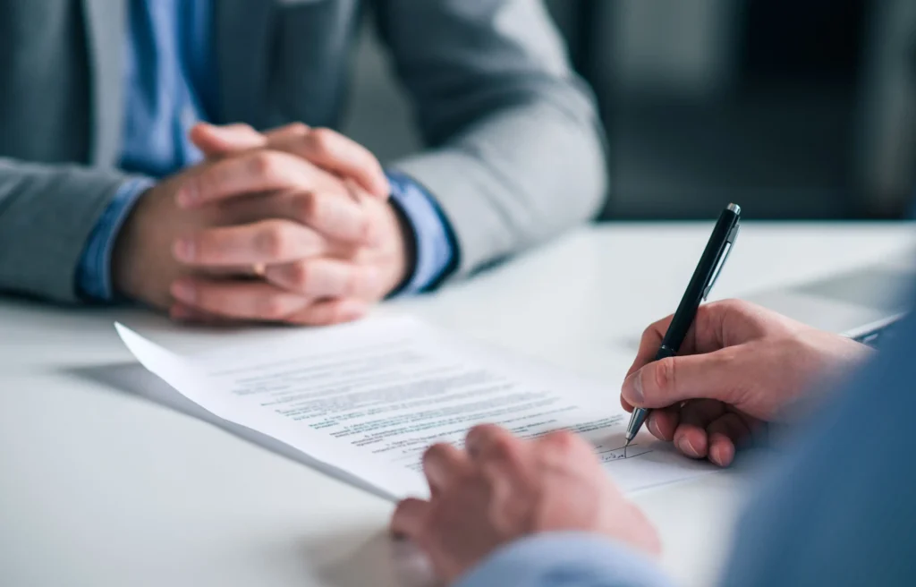 Close-up of a person signing an employment contract while relocating for a contract job.