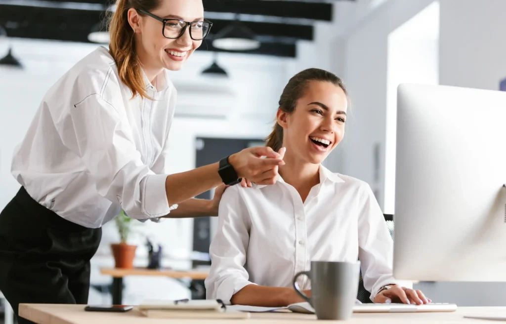 Employer guiding an intern while reviewing an intern relocation stipend on a desktop computer in the office.