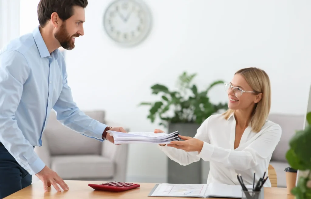 Man handing work documents to a female colleague as part of a relocation handover plan.