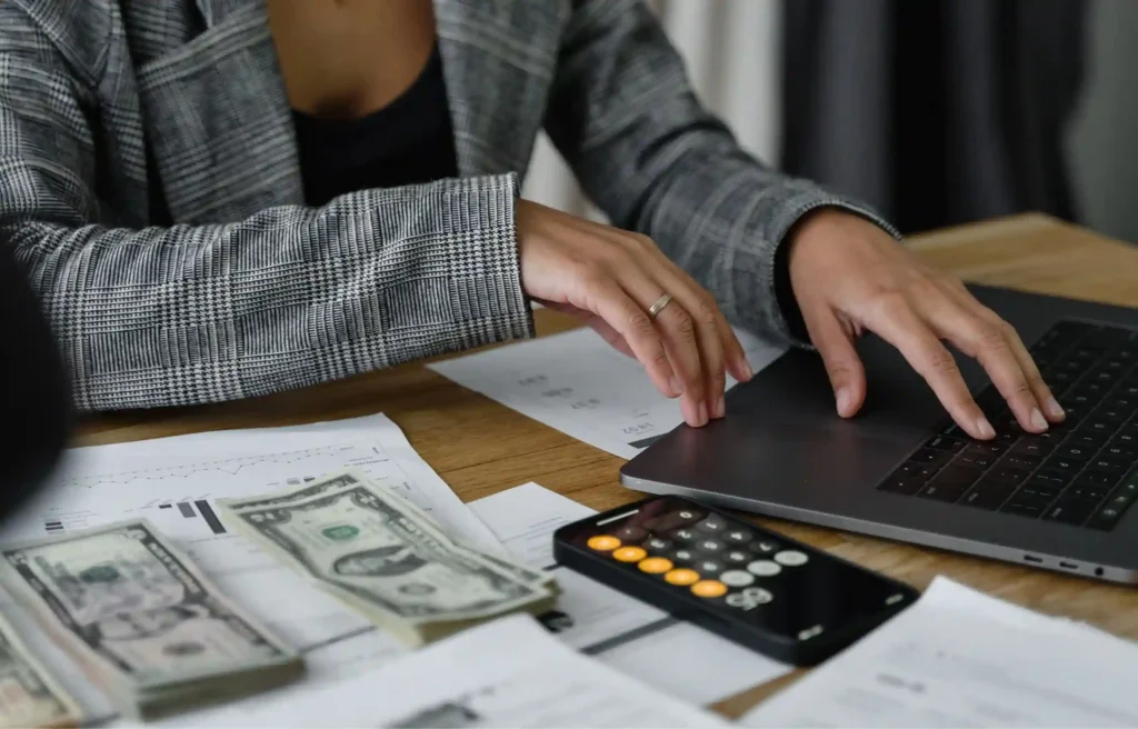 Person reviewing relocation rental market costs with cash, calculator, and laptop.
