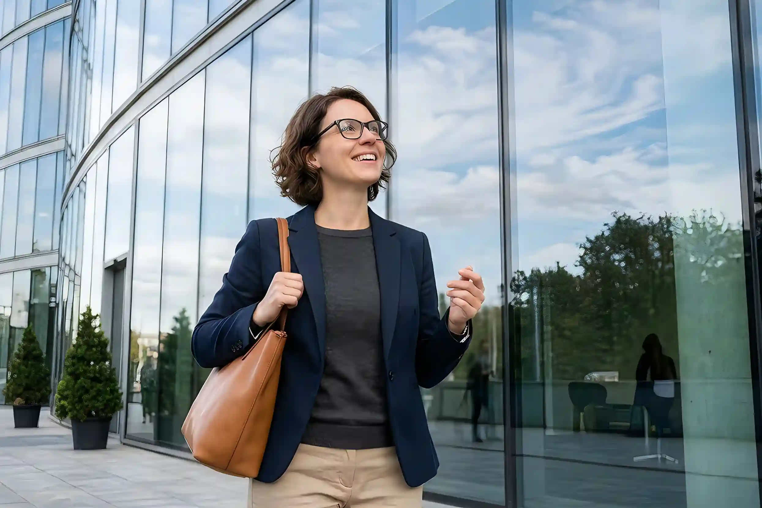 Professional woman carrying a shoulder bag outside a modern office building, representing employee relocation and career mobility.