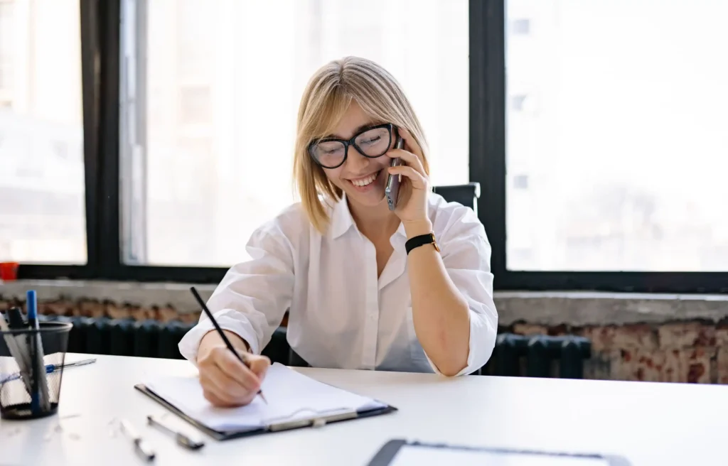Professional woman discussing exploding job offers by phone while reviewing and signing documents at her desk.