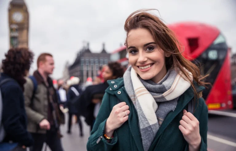 Young woman with a backpack standing near a red London bus in the city.